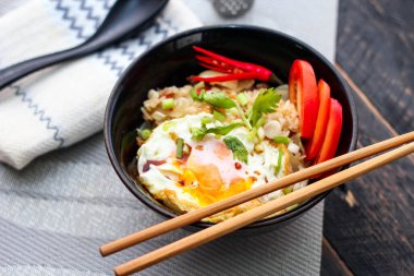 Japon usulü kızarmış pirinç, kızarmış yumurta ve kırmızı domates dilimleriyle birlikte siyah bir kasede servis ediliyor..