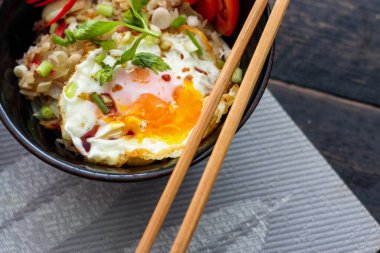 Japon usulü kızarmış pirinç, kızarmış yumurta ve kırmızı domates dilimleriyle birlikte siyah bir kasede servis ediliyor..