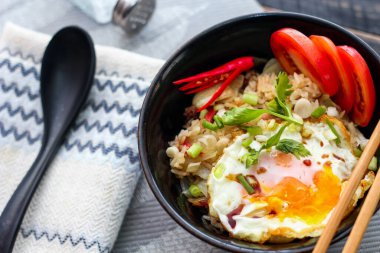 Japon usulü kızarmış pirinç, kızarmış yumurta ve kırmızı domates dilimleriyle birlikte siyah bir kasede servis ediliyor..