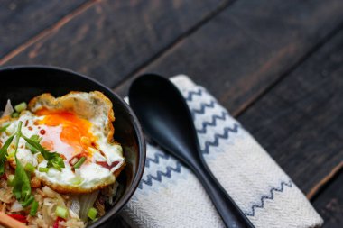 Japon usulü kızarmış pirinç, kızarmış yumurta ve kırmızı domates dilimleriyle birlikte siyah bir kasede servis ediliyor..