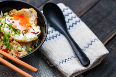 Japon usulü kızarmış pirinç, kızarmış yumurta ve kırmızı domates dilimleriyle birlikte siyah bir kasede servis ediliyor..