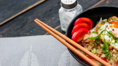 Japon usulü kızarmış pirinç, kızarmış yumurta ve kırmızı domates dilimleriyle birlikte siyah bir kasede servis ediliyor..