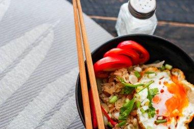 Japon usulü kızarmış pirinç, kızarmış yumurta ve kırmızı domates dilimleriyle birlikte siyah bir kasede servis ediliyor..