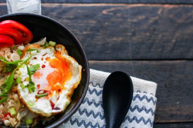 Japon usulü kızarmış pirinç, kızarmış yumurta ve kırmızı domates dilimleriyle birlikte siyah bir kasede servis ediliyor..