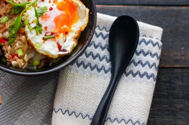 Japon usulü kızarmış pirinç, kızarmış yumurta ve kırmızı domates dilimleriyle birlikte siyah bir kasede servis ediliyor..