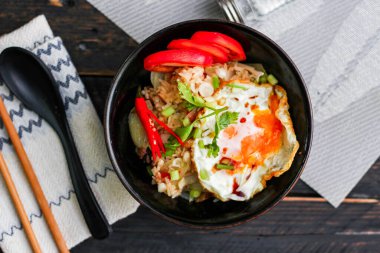 Japon usulü kızarmış pirinç, kızarmış yumurta ve kırmızı domates dilimleriyle birlikte siyah bir kasede servis ediliyor..