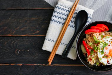 Japon usulü kızarmış pirinç, kızarmış yumurta ve kırmızı domates dilimleriyle birlikte siyah bir kasede servis ediliyor..