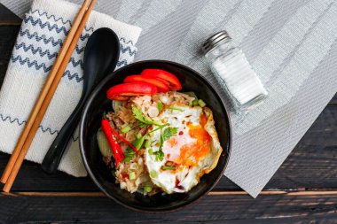 Japon usulü kızarmış pirinç, kızarmış yumurta ve kırmızı domates dilimleriyle birlikte siyah bir kasede servis ediliyor..