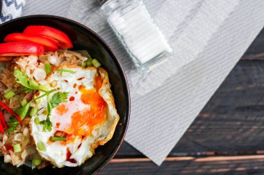 Japon usulü kızarmış pirinç, kızarmış yumurta ve kırmızı domates dilimleriyle birlikte siyah bir kasede servis ediliyor..