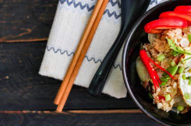 Japon usulü kızarmış pirinç, kızarmış yumurta ve kırmızı domates dilimleriyle birlikte siyah bir kasede servis ediliyor..