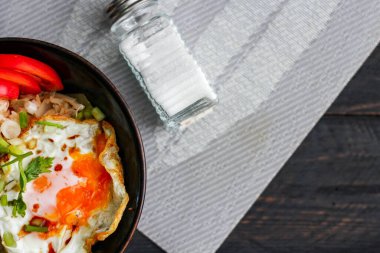 Japon usulü kızarmış pirinç, kızarmış yumurta ve kırmızı domates dilimleriyle birlikte siyah bir kasede servis ediliyor..