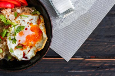 Japon usulü kızarmış pirinç, kızarmış yumurta ve kırmızı domates dilimleriyle birlikte siyah bir kasede servis ediliyor..