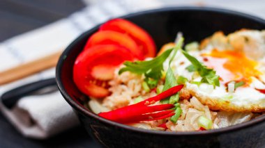 Japon usulü kızarmış pirinç, kızarmış yumurta ve kırmızı domates dilimleriyle birlikte siyah bir kasede servis ediliyor..