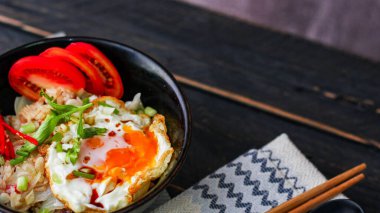 Japon usulü kızarmış pirinç, kızarmış yumurta ve kırmızı domates dilimleriyle birlikte siyah bir kasede servis ediliyor..