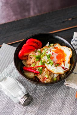 Japon usulü kızarmış pirinç, kızarmış yumurta ve kırmızı domates dilimleriyle birlikte siyah bir kasede servis ediliyor..