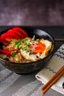 Japon usulü kızarmış pirinç, kızarmış yumurta ve kırmızı domates dilimleriyle birlikte siyah bir kasede servis ediliyor..