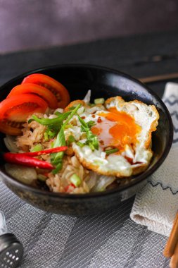 Japon usulü kızarmış pirinç, kızarmış yumurta ve kırmızı domates dilimleriyle birlikte siyah bir kasede servis ediliyor..