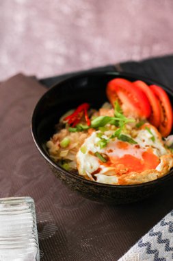 Japon usulü kızarmış pirinç, kızarmış yumurta ve kırmızı domates dilimleriyle birlikte siyah bir kasede servis ediliyor..