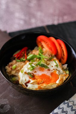 Japon usulü kızarmış pirinç, kızarmış yumurta ve kırmızı domates dilimleriyle birlikte siyah bir kasede servis ediliyor..