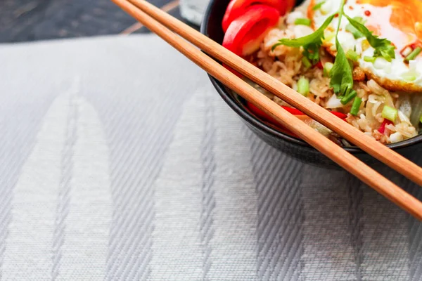 Japon usulü kızarmış pirinç, kızarmış yumurta ve kırmızı domates dilimleriyle birlikte siyah bir kasede servis ediliyor..