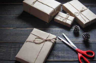 Kraft kağıdından hediye paketi sicimle sarılmış, el yapımı konsept, siyah ahşap masa üzerine yerleştirilmiş.