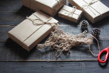 Kraft kağıdından hediye paketi sicimle sarılmış, el yapımı konsept, siyah ahşap masa üzerine yerleştirilmiş.