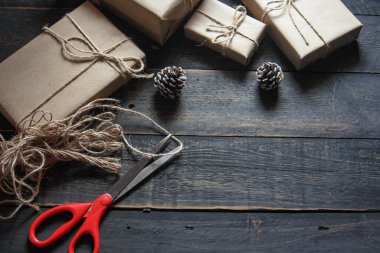 Kraft kağıdından hediye paketi sicimle sarılmış, el yapımı konsept, siyah ahşap masa üzerine yerleştirilmiş.