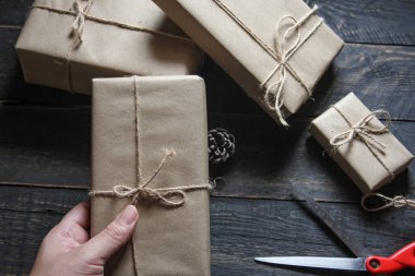 Kraft kağıdından hediye paketi sicimle sarılmış, el yapımı konsept, siyah ahşap masa üzerine yerleştirilmiş.