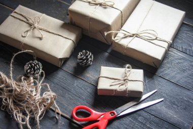 Kraft kağıdından hediye paketi sicimle sarılmış, el yapımı konsept, siyah ahşap masa üzerine yerleştirilmiş.