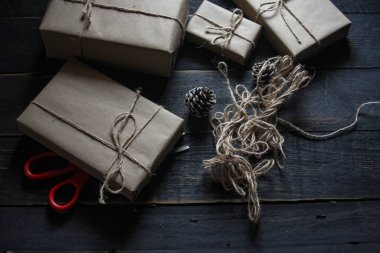 Kraft kağıdından hediye paketi sicimle sarılmış, el yapımı konsept, siyah ahşap masa üzerine yerleştirilmiş.