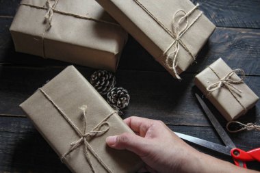 Kraft kağıdından hediye paketi sicimle sarılmış, el yapımı konsept, siyah ahşap masa üzerine yerleştirilmiş.