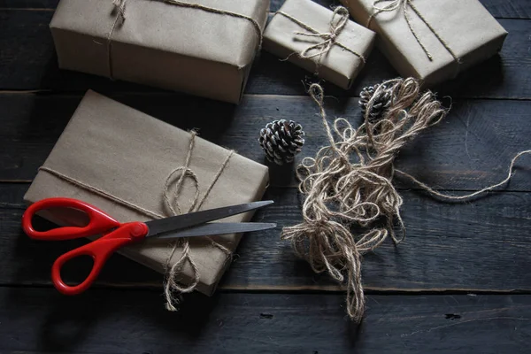 Kraft kağıdından hediye paketi sicimle sarılmış, el yapımı konsept, siyah ahşap masa üzerine yerleştirilmiş.