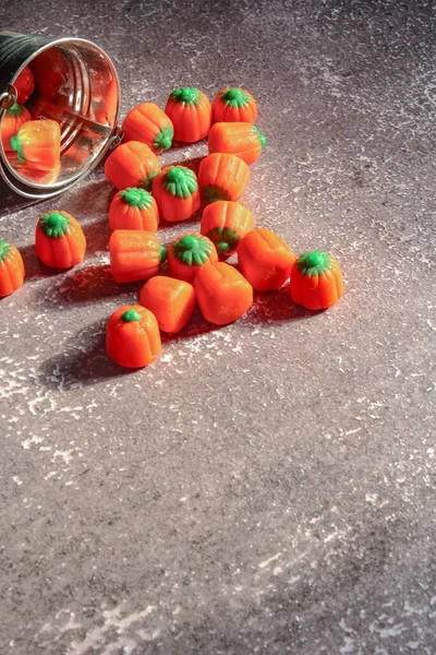 Halloween-colored pumpkin-shaped candy canes are placed on a gray table with sunlight in the background.