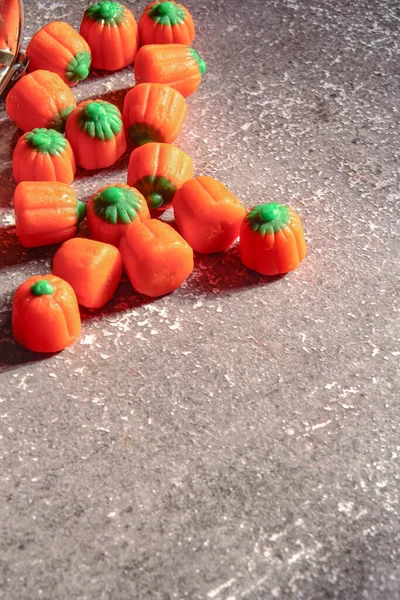 Halloween-colored pumpkin-shaped candy canes are placed on a gray table with sunlight in the background.
