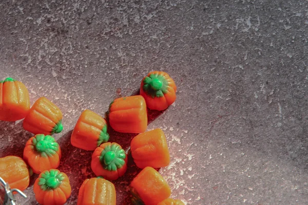Halloween-colored pumpkin-shaped candy canes are placed on a gray table with sunlight in the background.