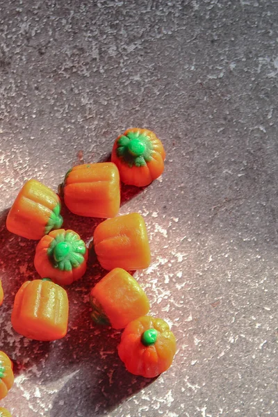 Halloween-colored pumpkin-shaped candy canes are placed on a gray table with sunlight in the background.