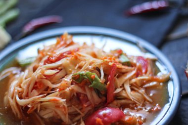 Baharatlı papaya salatası mavi bir tabakta, kovada pilav ve uzun fasulye, kurutulmuş kırmızı biber ve sebze ile servis edilir..