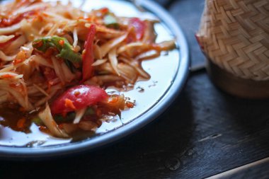 Baharatlı papaya salatası mavi bir tabakta, kovada pilav ve uzun fasulye, kurutulmuş kırmızı biber ve sebze ile servis edilir..