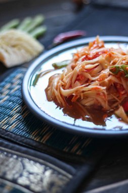 Baharatlı papaya salatası mavi bir tabakta, kovada pilav ve uzun fasulye, kurutulmuş kırmızı biber ve sebze ile servis edilir..