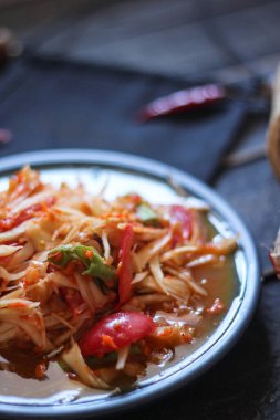 Baharatlı papaya salatası mavi bir tabakta, kovada pilav ve uzun fasulye, kurutulmuş kırmızı biber ve sebze ile servis edilir..