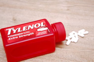 Va-USA 12-03-2025 Kırmızı Tylenol Ekstra Güçlü bir şişe, ahşap bir yüzey üzerinde uzanır Birkaç beyaz kapsül tezgah ve günlük sağlık hizmetleri üzerine yakın renklendirilmiş.