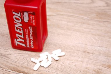 Va-USA 12-03-2025 Kırmızı Tylenol Ekstra Güçlü bir şişe, ahşap bir yüzey üzerinde uzanır Birkaç beyaz kapsül tezgah ve günlük sağlık hizmetleri üzerine yakın renklendirilmiş.