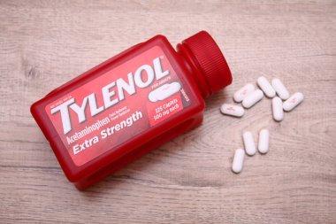Va-USA 12-03-2025 Kırmızı Tylenol Ekstra Güçlü bir şişe, ahşap bir yüzey üzerinde uzanır Birkaç beyaz kapsül tezgah ve günlük sağlık hizmetleri üzerine yakın renklendirilmiş.