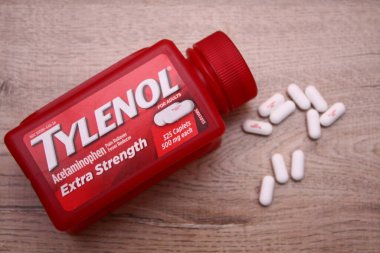 Va-USA 12-03-2025 Kırmızı Tylenol Ekstra Güçlü bir şişe, ahşap bir yüzey üzerinde uzanır Birkaç beyaz kapsül tezgah ve günlük sağlık hizmetleri üzerine yakın renklendirilmiş.