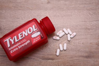Va-USA 12-03-2025 Kırmızı Tylenol Ekstra Güçlü bir şişe, ahşap bir yüzey üzerinde uzanır Birkaç beyaz kapsül tezgah ve günlük sağlık hizmetleri üzerine yakın renklendirilmiş.
