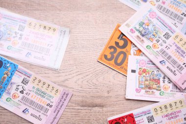 Bangkok, Tayland 18 Haziran 2025, Tayland piyango biletlerinin bir koleksiyonu ahşap bir yüzeyde, renkli tasarımlar sergileniyor, seri numaraları ve bilgi çekiliyor.