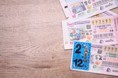 Bangkok, Tayland 18 Haziran 2025, Tayland piyango biletlerinin bir koleksiyonu ahşap bir yüzeyde, renkli tasarımlar sergileniyor, seri numaraları ve bilgi çekiliyor.