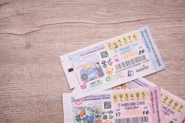 Bangkok, Tayland 18 Haziran 2025, Tayland piyango biletlerinin bir koleksiyonu ahşap bir yüzeyde, renkli tasarımlar sergileniyor, seri numaraları ve bilgi çekiliyor.