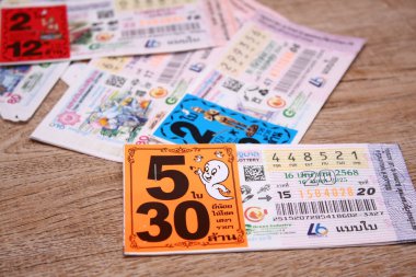 Bangkok, Tayland 18 Haziran 2025, Tayland piyango biletlerinin bir koleksiyonu ahşap bir yüzeyde, renkli tasarımlar sergileniyor, seri numaraları ve bilgi çekiliyor.