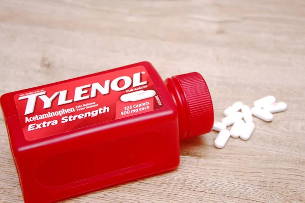 Va-USA 12-03-2025 Kırmızı Tylenol Ekstra Güçlü bir şişe, ahşap bir yüzey üzerinde uzanır Birkaç beyaz kapsül tezgah ve günlük sağlık hizmetleri üzerine yakın renklendirilmiş.
